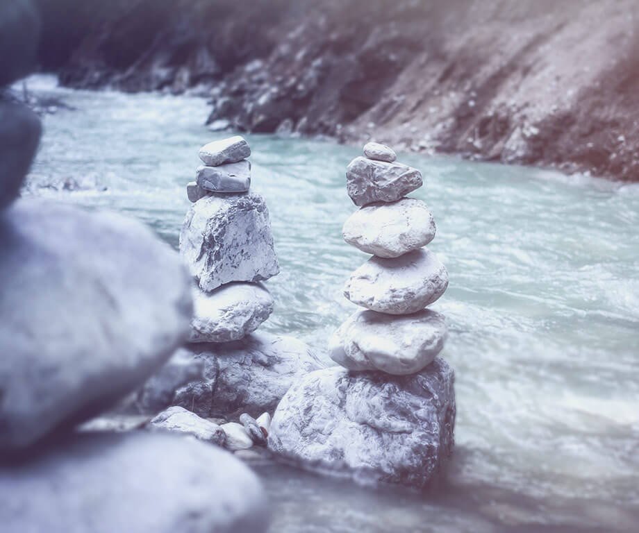 River in the mountains, in the foreground two cairns, a third cairn out of focus