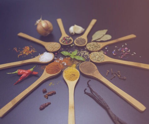 Nine wooden spoons with different TCM spices on dark background