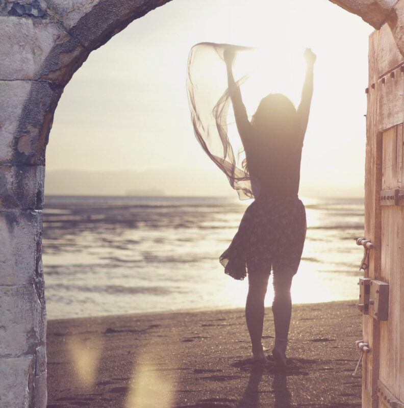Woman on beach at sunset photographed through old open door