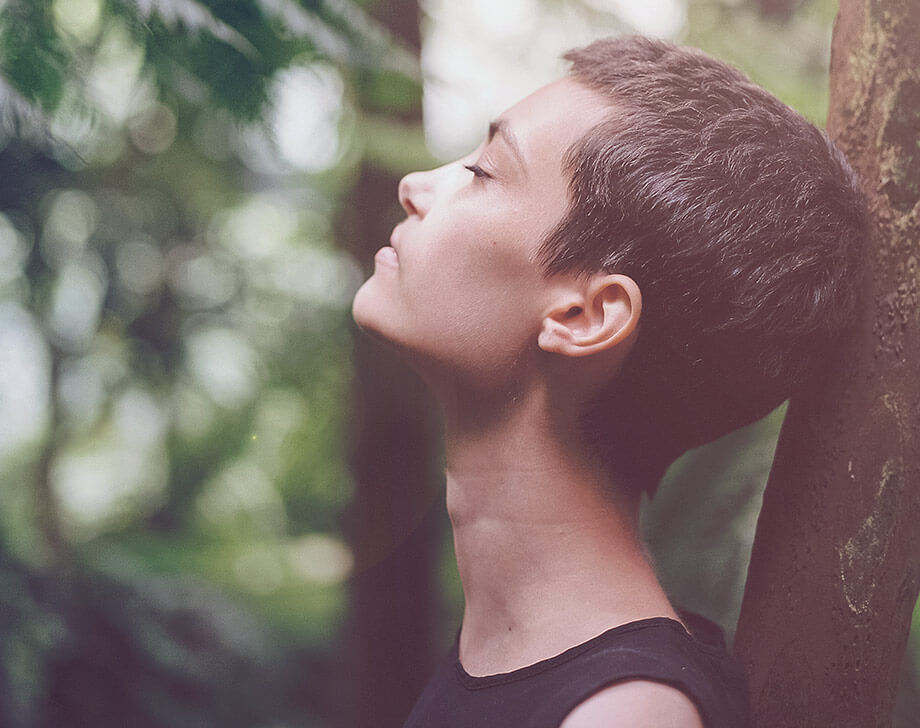 Woman in forest, looking up relaxed with closed eyes
