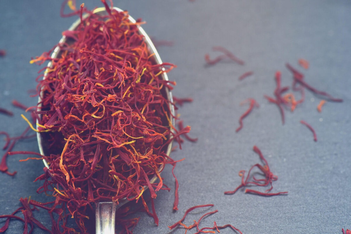 Spoon filled with saffron threads, some saffron threads lie on the table to the right of the spoon