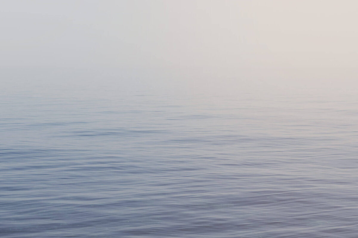 Calm water surface of a big lake, fog in the background.