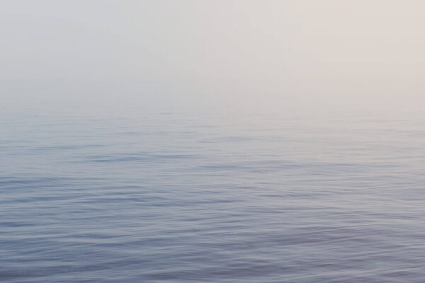 Calm water surface of a big lake, fog in the background.