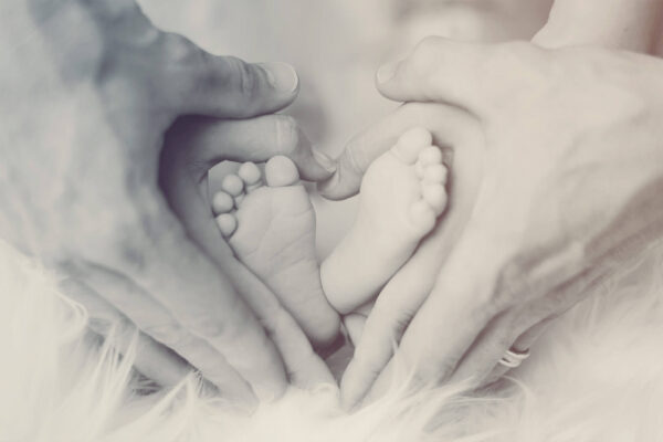 Hands of two adults form a heart, in the middle the feet of a young baby