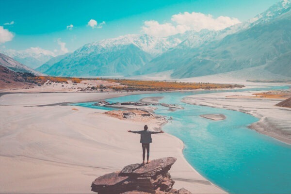 Man stands with outstretched arms on a large stone and looks at a river landscape