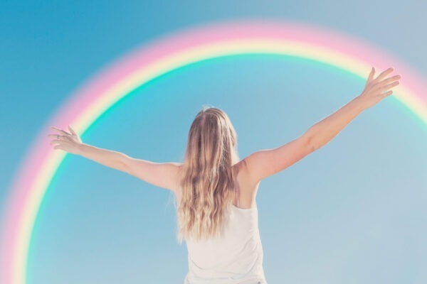 Woman with outstretched arms in front of rainbow